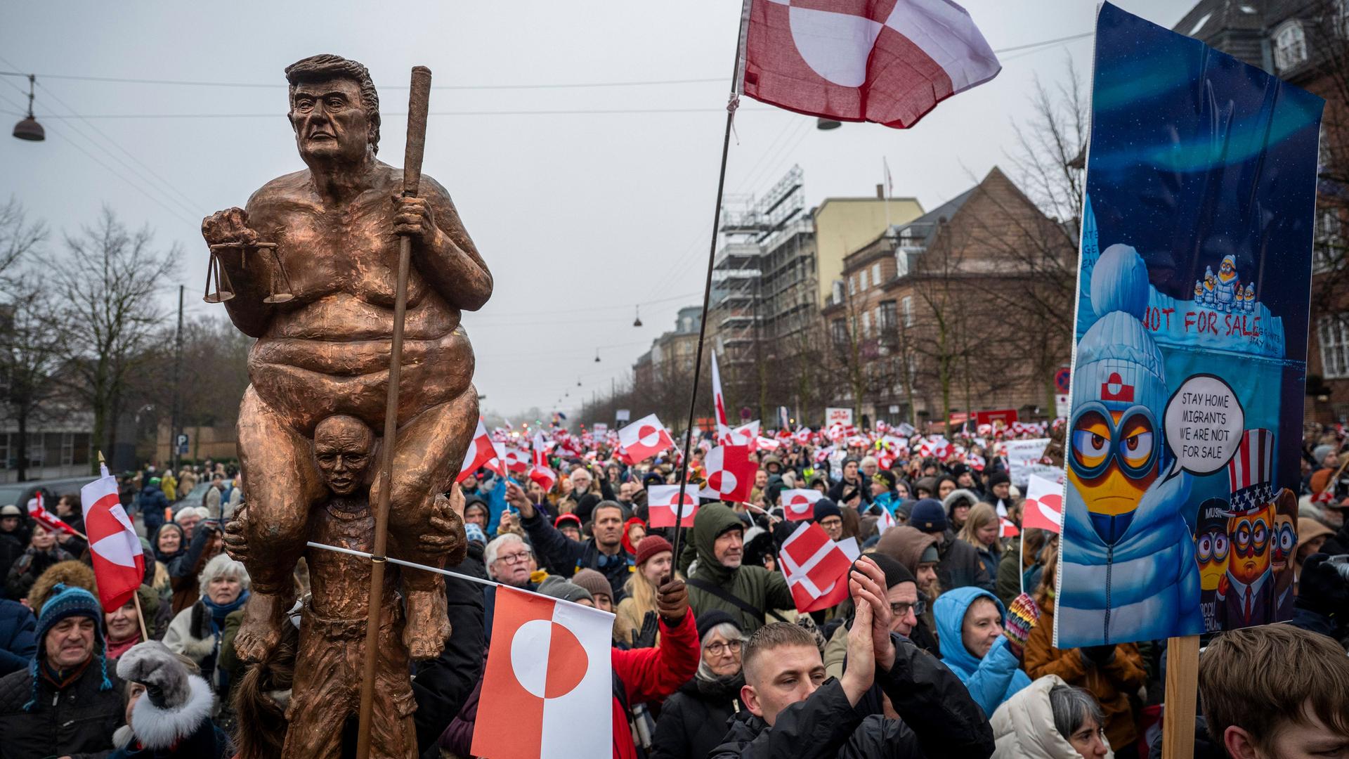 Eine große Menschenmenge mit rot-weißen Fahnen läuft durch eine Straße. Eine Person trägt eine Statue, die US-Präsident Trump darstellen soll.