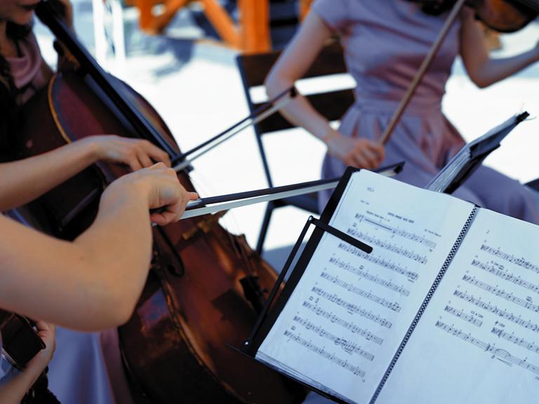 Musiker und Musikerinnen spielen draußen Streichinstrumente