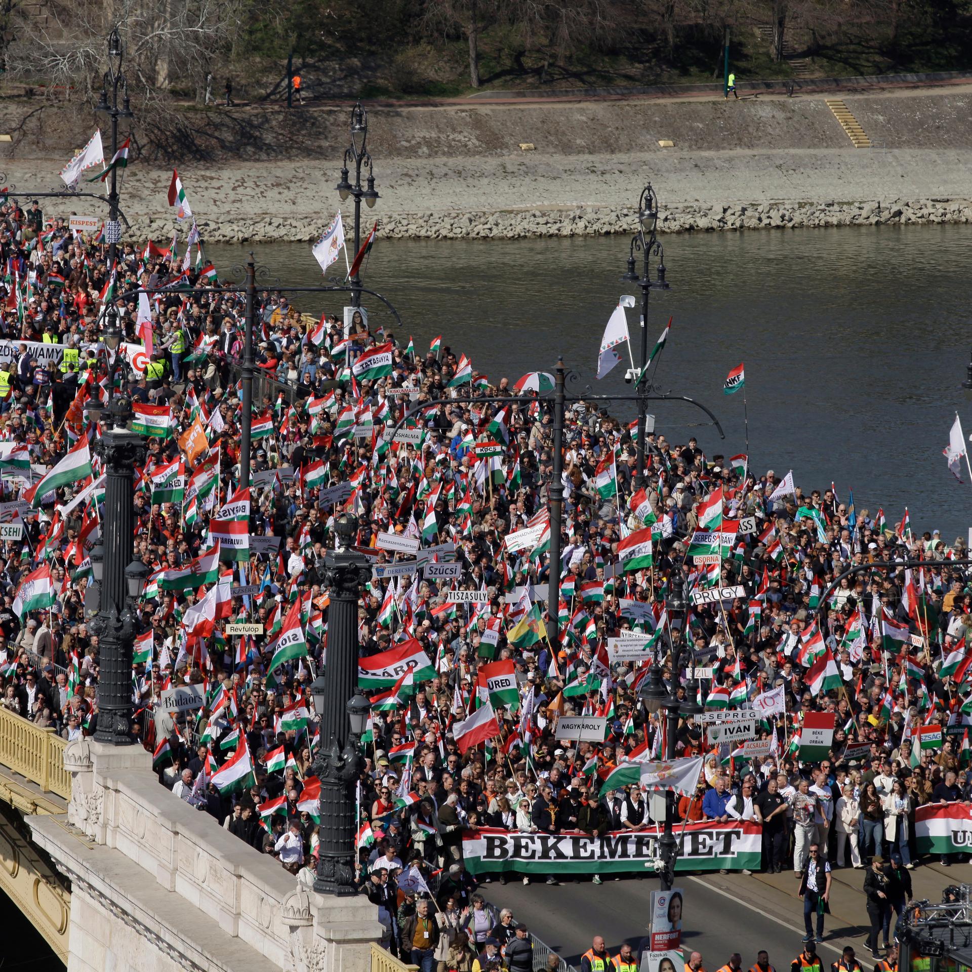 Tausende Menschen ziehen mit Fahnen und Bannern bei einem Demonstrationszug über eine Brücke in Ungarns Hauptstadt Budapest.