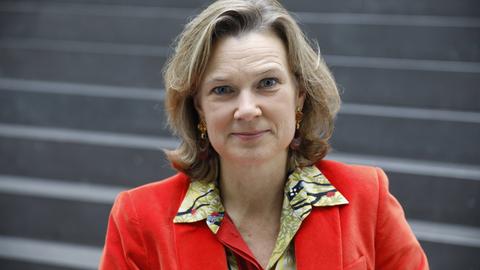 Katharina von Schnurbein trägt einen roten Blazer und darunter eine bunt gemusterte Bluse. Sie blickt lächelnd in die Kamera.