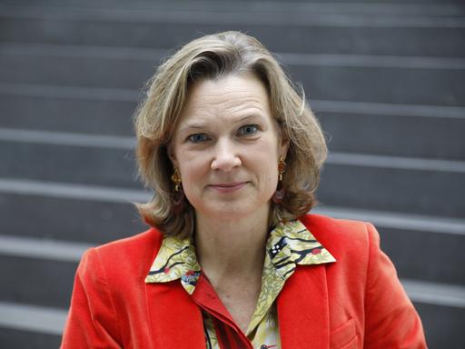 Katharina von Schnurbein trägt einen roten Blazer und darunter eine bunt gemusterte Bluse. Sie blickt lächelnd in die Kamera.